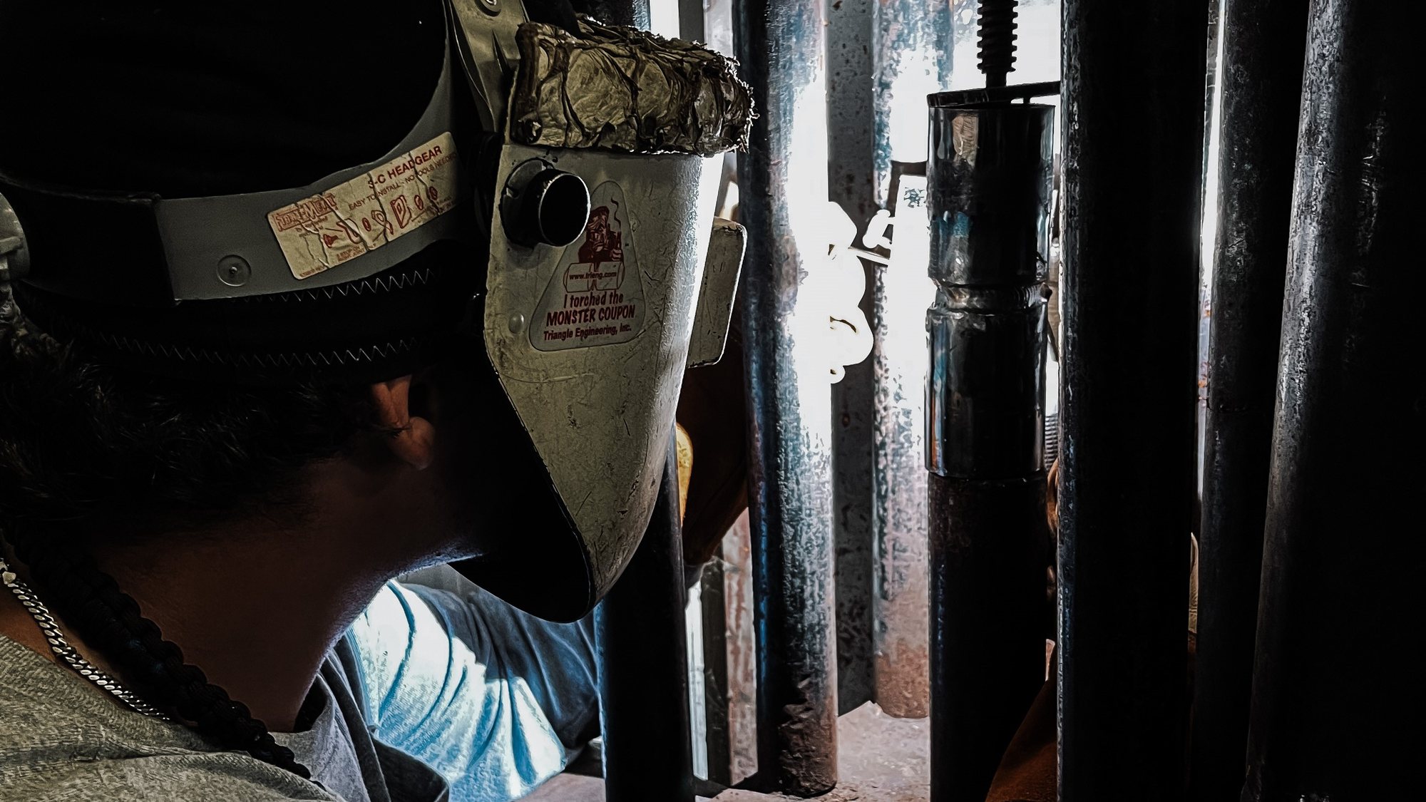 A KWI student welding in a booth beside racked pipe on the training shop floor